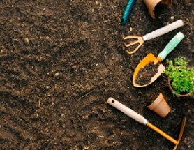 Four landscaping and gardening tools lying in a garden filled with dirt.