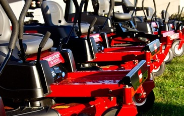 Professional lawn mowing equipment and mowers lined up on a well trimmed green grass landscape.